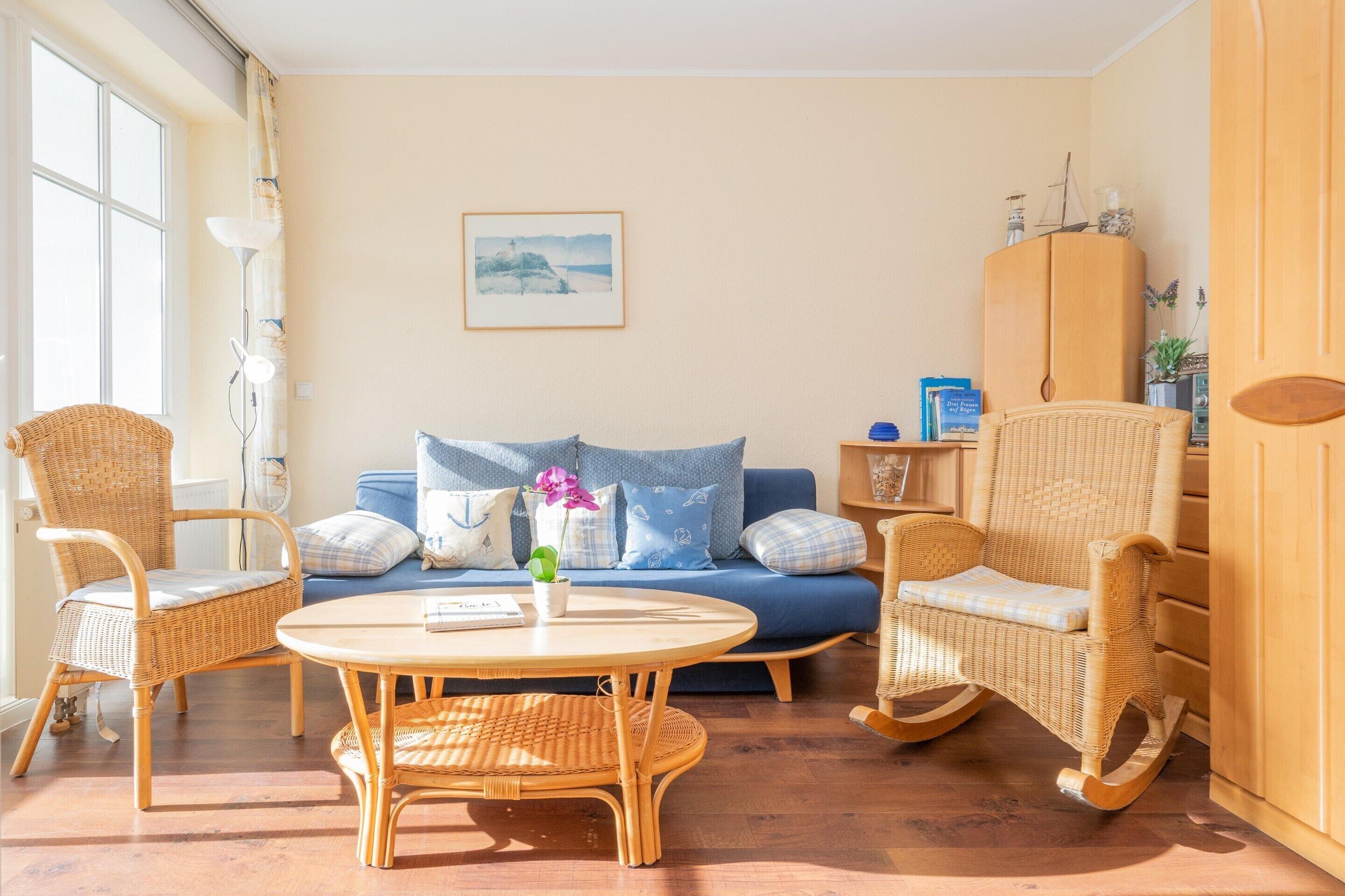 A living room with a blue sofa, wicker chairs, a round table, and a wooden cabinet.