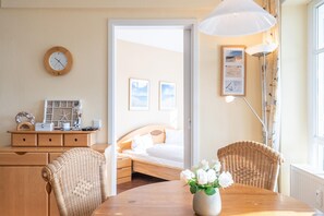 A room with a bed, a dining table with chairs, a lamp, a clock, and framed pictures on the wall. - Ferienwohnung im 1.og mit Balkon in Sellin (Sellin)