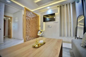 A modern living room with a wooden coffee table, a TV mounted on the wall, and a decorative partition. - Appart moderne -Confort premium près de Guéliz (Marrakech)