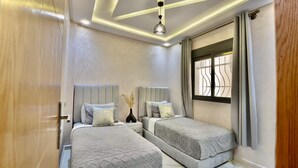 A bedroom with two beds, a nightstand, a decorative vase, and a window with curtains. - Appart moderne -Confort premium près de Guéliz (Marrakech)