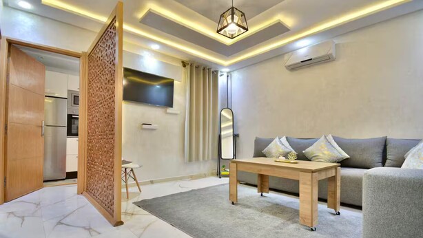 A modern living room with a sofa, a coffee table, a TV, and a decorative partition. - Appart moderne -Confort premium près de Guéliz (Marrakech)