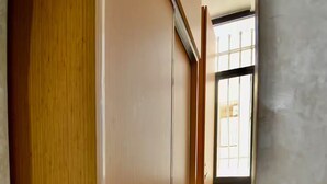 A narrow hallway with a wooden door on the left, a window with metal bars on the right, and a tiled floor. - Appart moderne -Confort premium près de Guéliz (Marrakech)