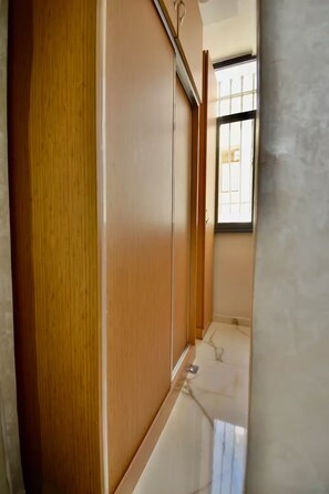 A narrow hallway with a wooden door on the left, a window with metal bars on the right, and a tiled floor. - Appart moderne -Confort premium près de Guéliz (Marrakech)