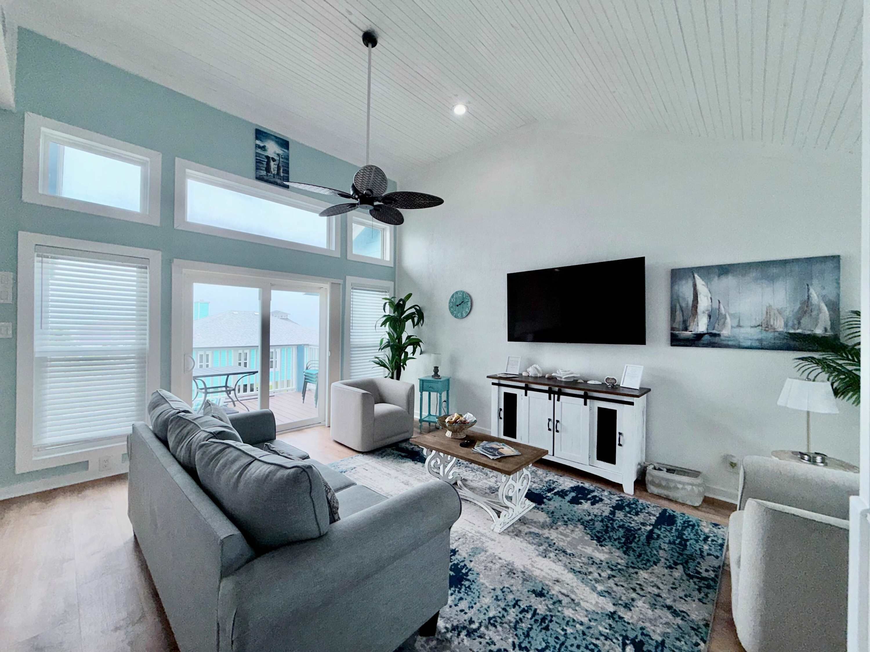 A spacious living room with a grey sofa, a coffee table, and a large window overlooking a balcony.