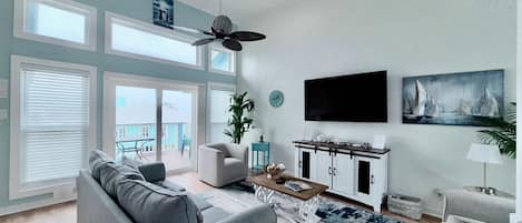A spacious living room with a grey sofa, a coffee table, and a large window overlooking a balcony.