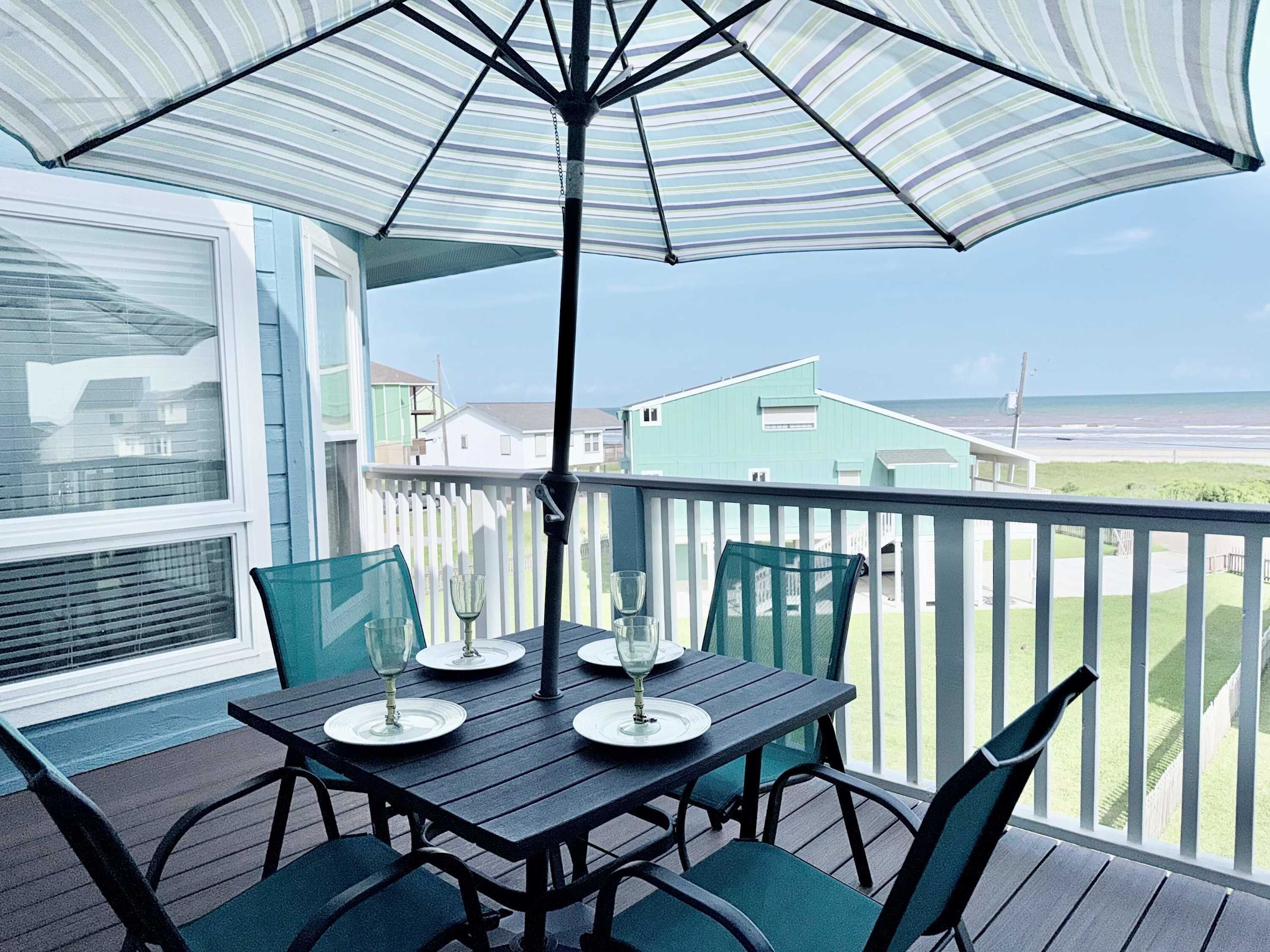 A covered outdoor dining area with a table and chairs, an umbrella, and a view of the ocean.