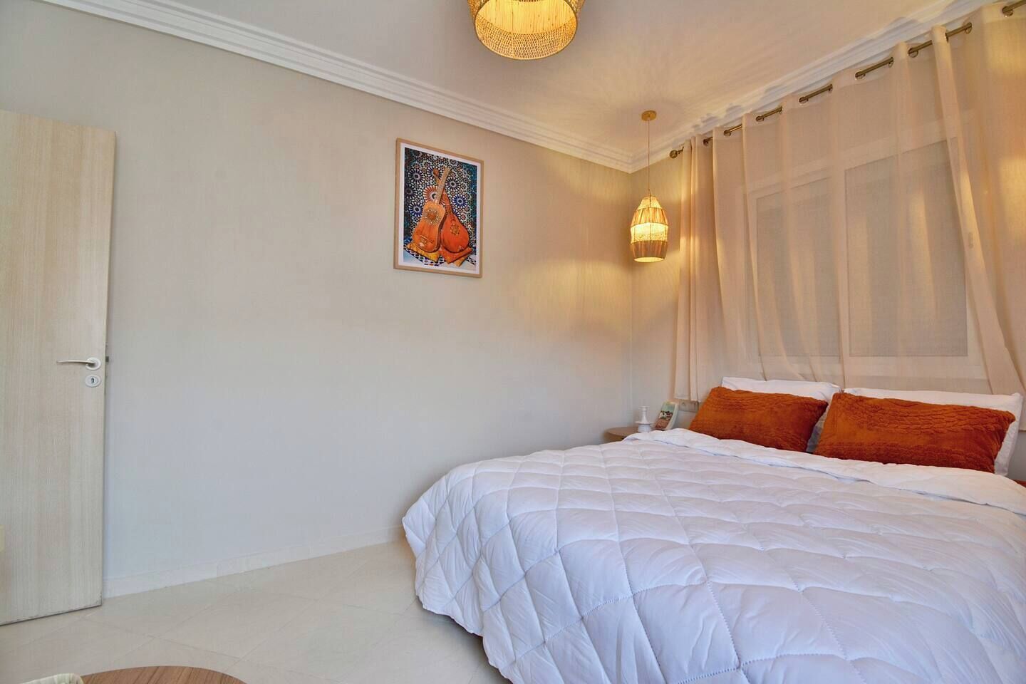 A bedroom with a bed, a door, a wall-mounted light, and a painting.