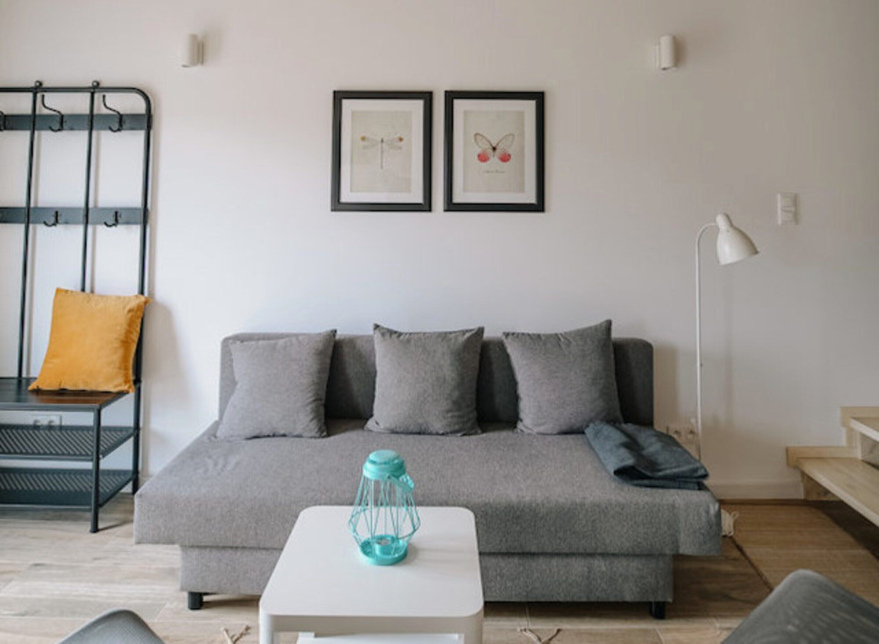 A modern living room with a grey sofa, a small white table, a teal lantern, and two framed pictures on the wall.