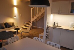 A modern kitchen with white cabinets, a dining area with a table and chairs, and a staircase leading to another level. - Holiday Home With Terrace, Large Garden (Choczewo)