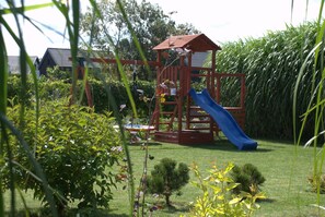 A playground with a slide and climbing structure, surrounded by greenery and a hedge. - Holiday Home With Terrace, Large Garden (Choczewo)