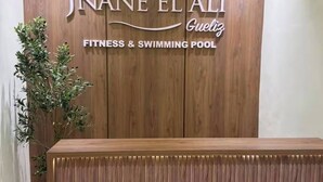 Een receptiebalie met een houten paneelwand waarop de naam 'JNANE EL ALI' staat, samen met de woorden 'FITNESS & ZWEMBAD'.