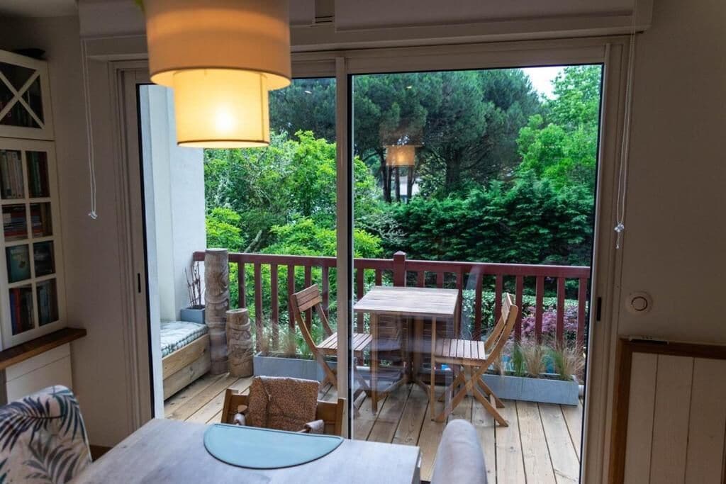 A room with a sliding glass door leading to a deck, a table with chairs, a cushioned bench, and a hanging light fixture.