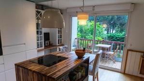 Una cocina moderna con una isla de madera, un comedor con mesa y sillas, y vistas a la vegetación a través de un ventanal corredero.