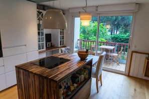A modern kitchen with a wooden island, a dining area with a table and chairs, and a view of greenery through a sliding glass door. - Me Lady's Cocoon 3-Star (Capbreton)