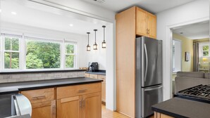A modern kitchen with wooden cabinets, a stainless steel refrigerator, a gas stove, and pendant lighting.