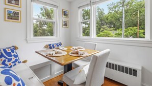 A dining area with a table set for four, white walls, and large windows with a view of greenery.