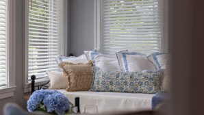 A room with a bed, white blinds, and a window with a view of trees.