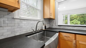 A modern kitchen with a stainless steel sink, wooden cabinets, and a window with blinds.
