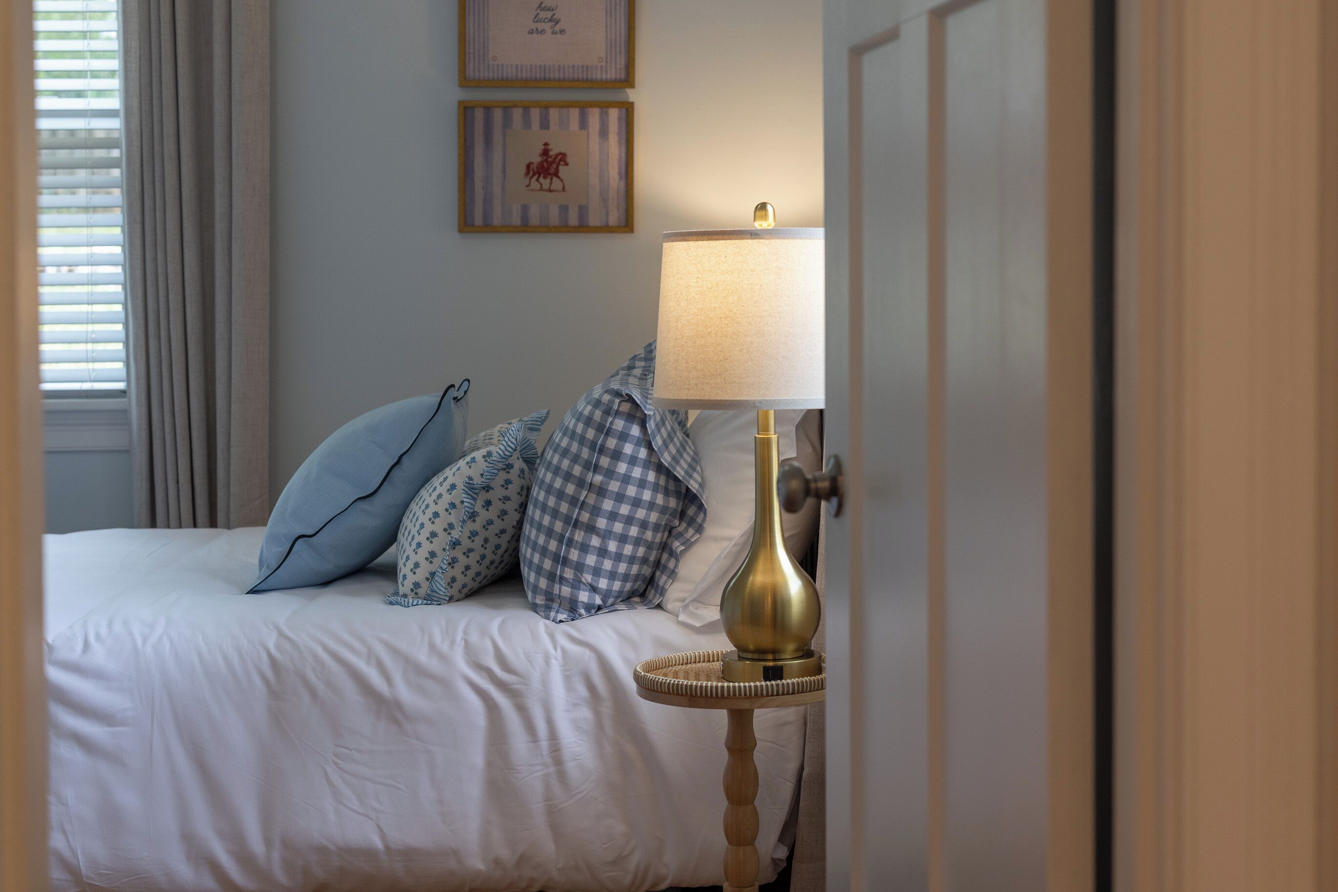 A neatly made bed with patterned pillows, a brass table lamp, and two framed pictures on the wall.