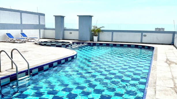 Una piscina en la azotea con un diseño de mosaicos de cuadros, algunas sillas de descanso y una planta en maceta.