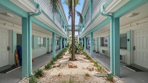 A corridor with a central tree, white doors, and teal pillars. - Turquoise Dream  One bedroom Condo On Pass a Grille Beach (St. Pete Beach)
