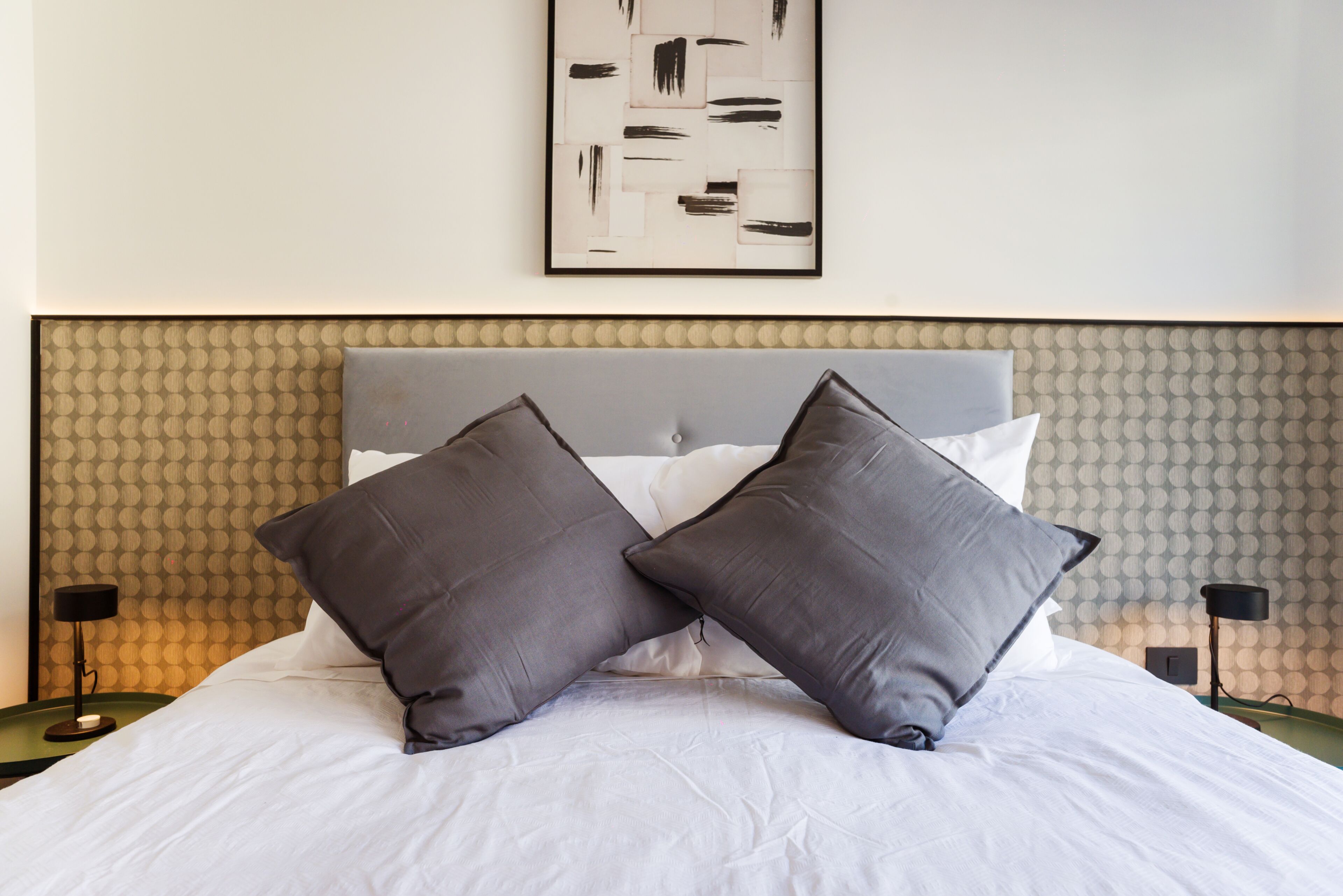 Una cama bien hecha con dos almohadas, un cabecero y una pared con un diseño texturizado.