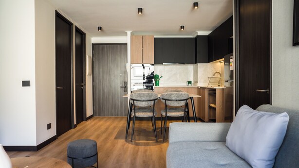 Una cucina moderna con mobili scuri, un'area pranzo con due sedie e un divano grigio in un soggiorno.