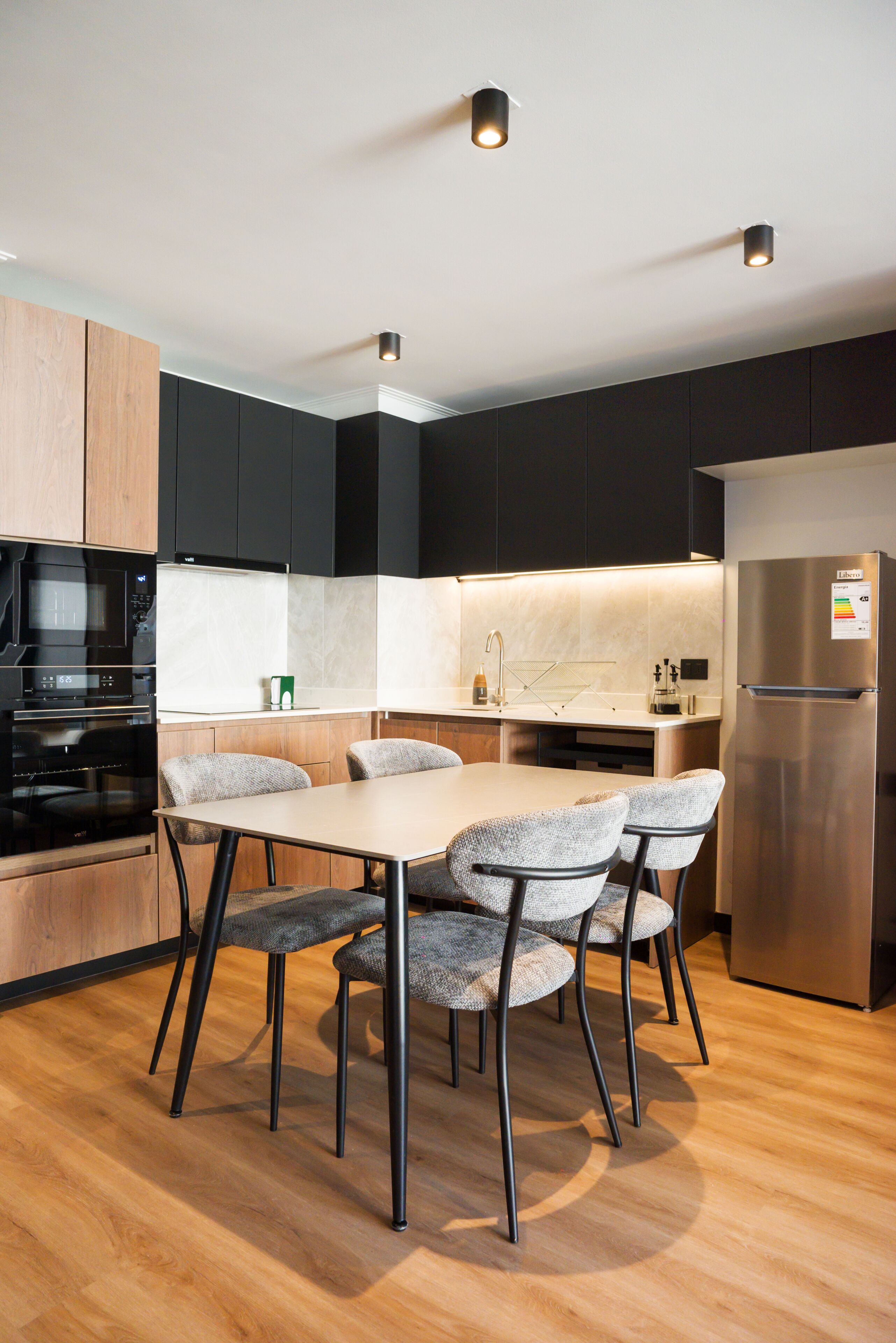 A modern kitchen with a dining table and chairs, a refrigerator, and a built-in oven.