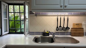 Una cocina con un lavamanos de acero inoxidable, armarios blancos, salpicadero azulejado y utensilios de cocina colgantes.