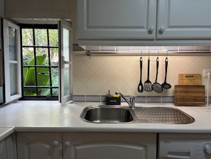 A kitchen with a stainless steel sink, white cabinets, a tiled backsplash, and hanging kitchen utensils. - Bright apartment in Alfama, right in the heart of Lisbon and fado music. (Lisboa)