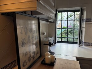 A kitchen with a framed botanical illustration, a coffee machine, and a window with a view of greenery. - Bright apartment in Alfama, right in the heart of Lisbon and fado music. (Lisboa)
