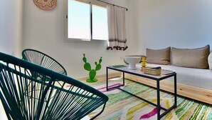 Ein modernes Wohnzimmer mit einer Couch, zwei Sesseln, einem Couchtisch, einer Sukkulente als Dekoration und einem Fenster mit Vorhängen.