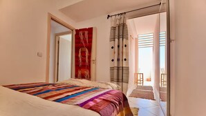 Ein Schlafzimmer mit einem Bett, einem roten Dekorationsgegenstand, einem Fenster mit Vorhängen und Blick ins Freie.