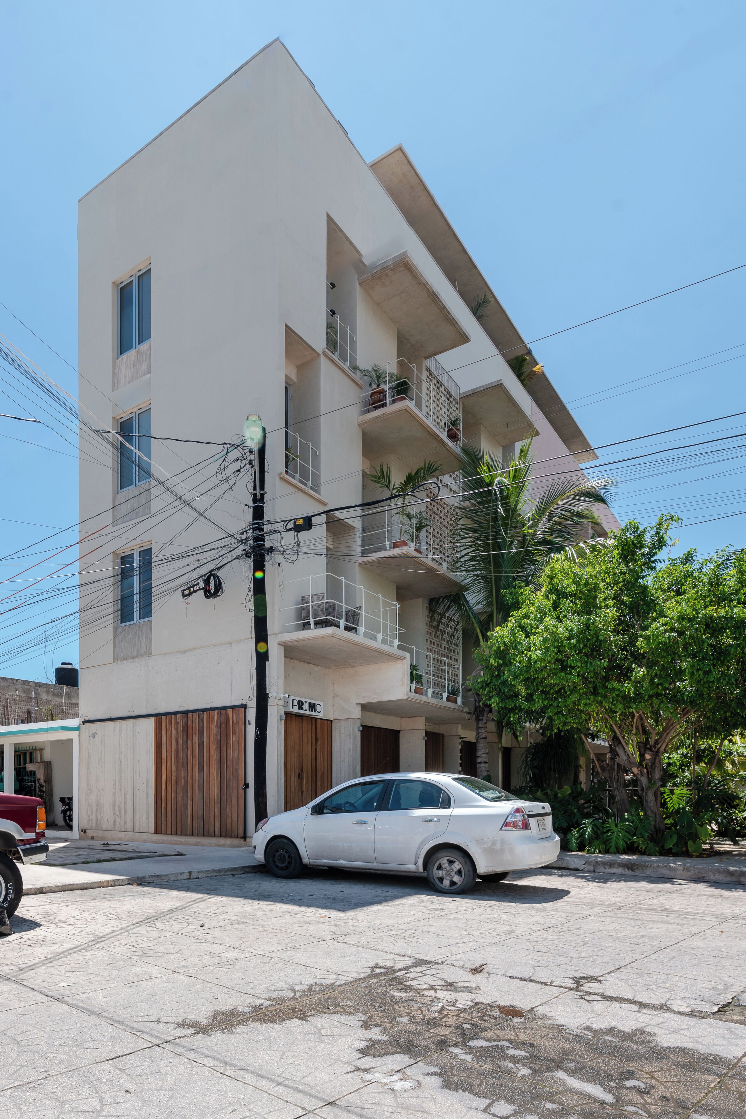 A multi-story building with balconies, a car parked in front, and a utility pole with wires.