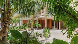 Un patio con palmeras, plantas en macetas y un edificio con puertas de madera y un balcón.