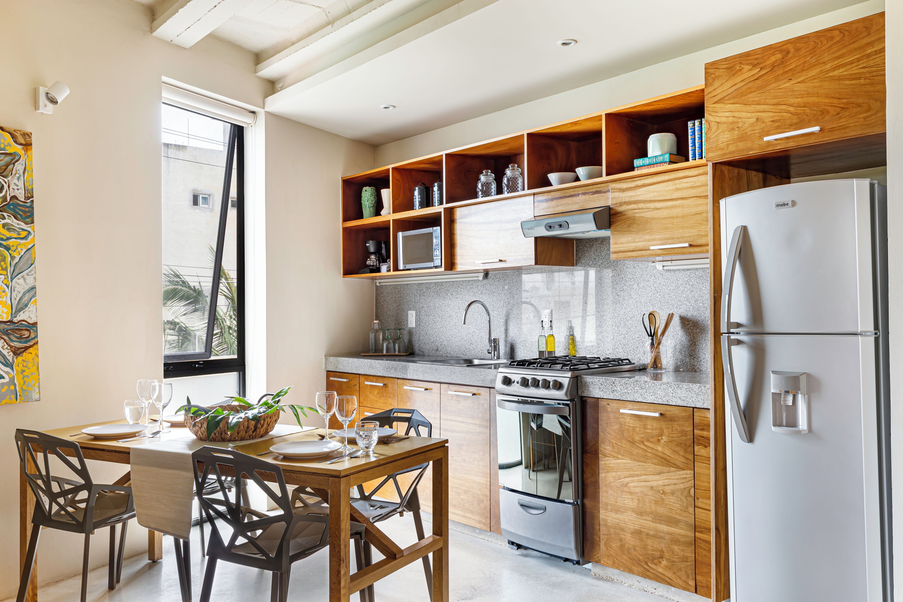 A modern kitchen with wooden cabinets, a stainless steel refrigerator, and a dining area with a table and chairs.