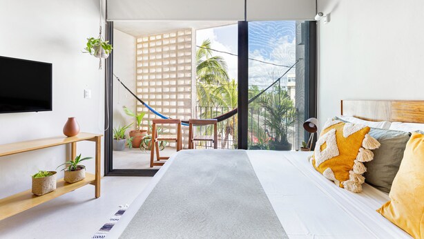 Un dormitorio moderno con una cama, televisión, hamaca y balcón con plantas.