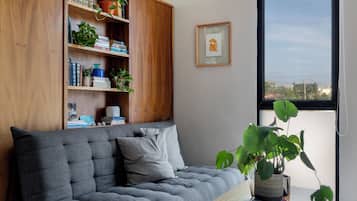 Una sala de estar moderna con un sofá gris, una estantería de madera y una ventana con vistas a edificios.