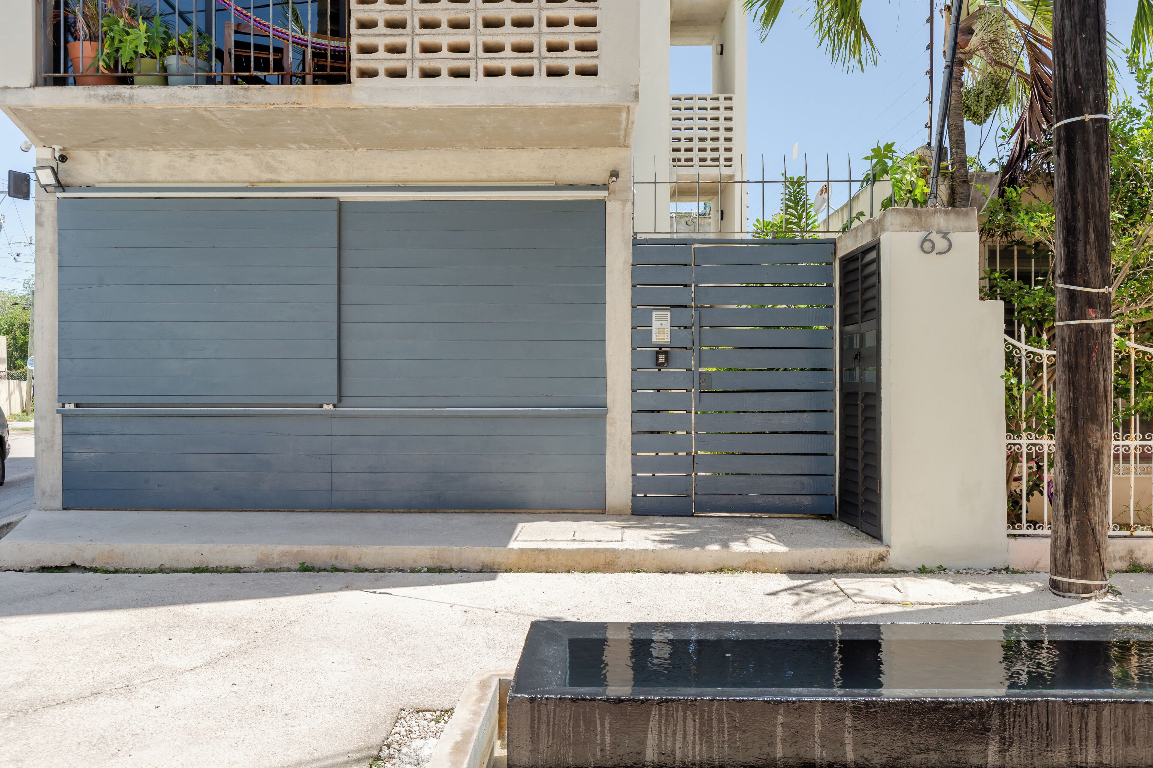Un edificio moderno con una puerta de garaje cerrada, una entrada con portones y una jardinera de concreto con fuente de agua.