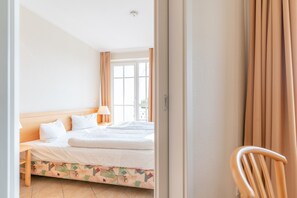 A hotel room with a bed, a nightstand, a lamp, a chair, and a window with curtains. - Ferienwohnung mit Badewanne auf Rugen (Sellin)