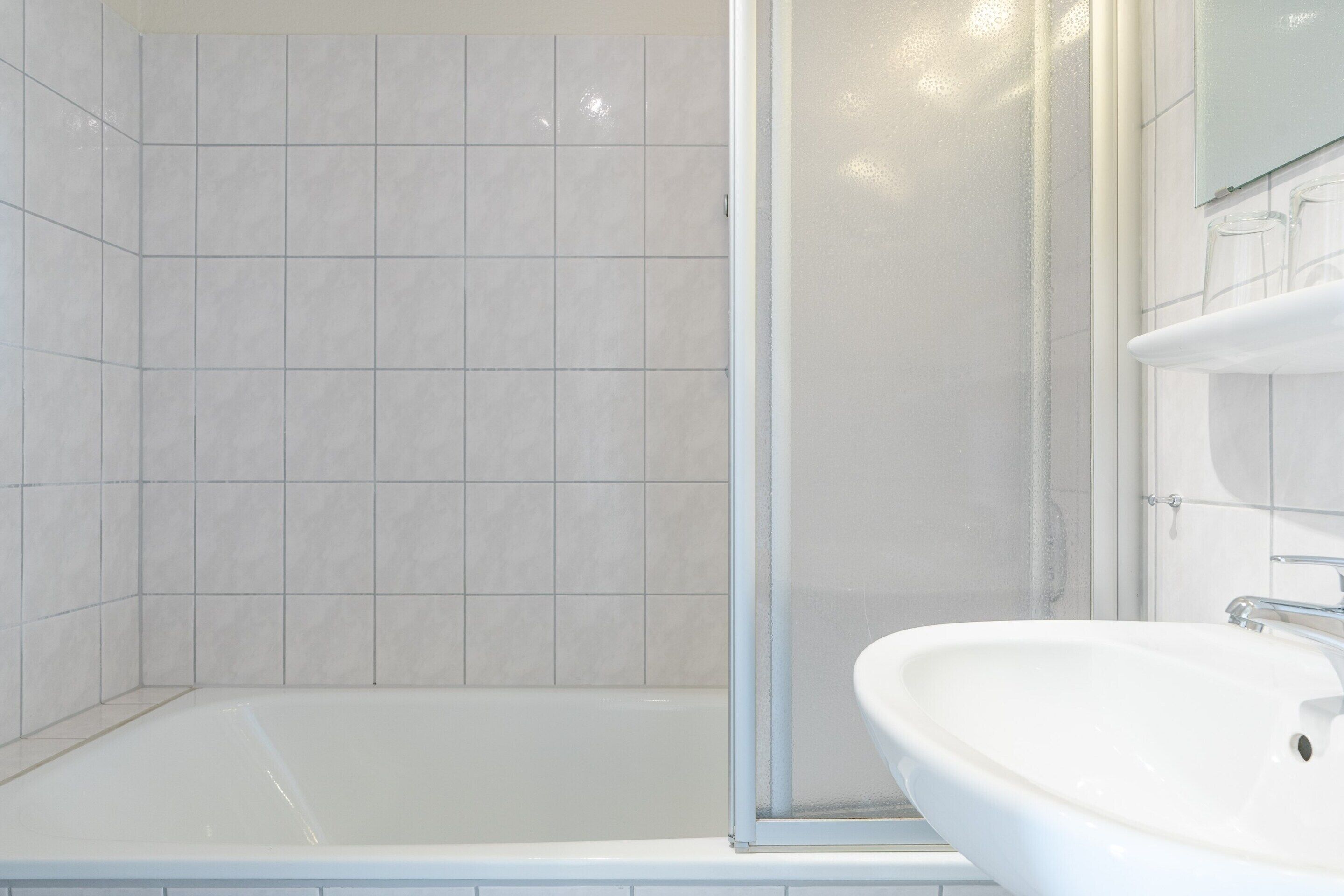 Un bagno moderno con una vasca da bagno bianca, uno box doccia in vetro e un lavandino bianco.