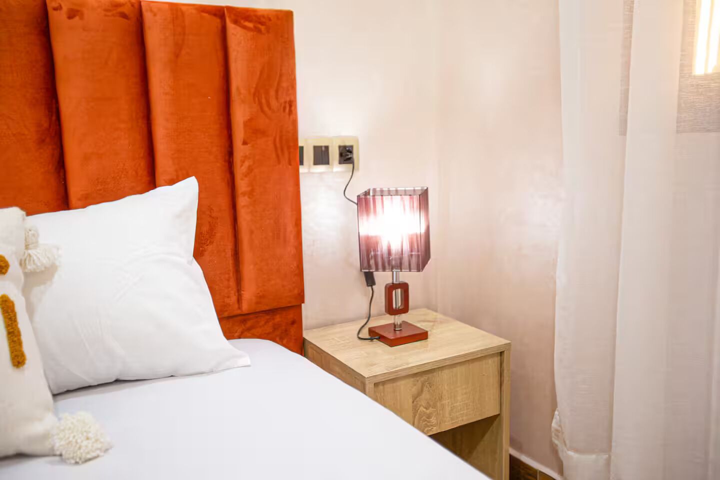 Una camera d'albergo con un letto, un comodino con una lampada e una testiera in legno.
