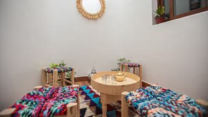 Une pièce chaleureuse avec une table ronde en bois, deux chaises, une petite plante en pot, un miroir et un tapis coloré tissé.