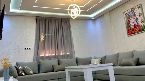 Un salon moderne avec un canapé d’angle, une table basse et un plafond doté d’un éclairage aux motifs géométriques.