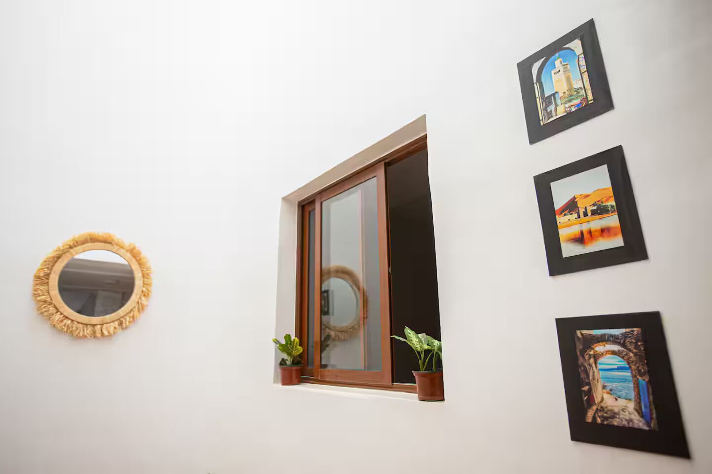 Une pièce avec un miroir rond, une fenêtre à cadre en bois et trois tableaux encadrés accrochés au mur.
