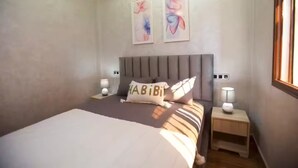 Une chambre à coucher avec un lit, deux tables de chevet, des œuvres d’art murales et une fenêtre.