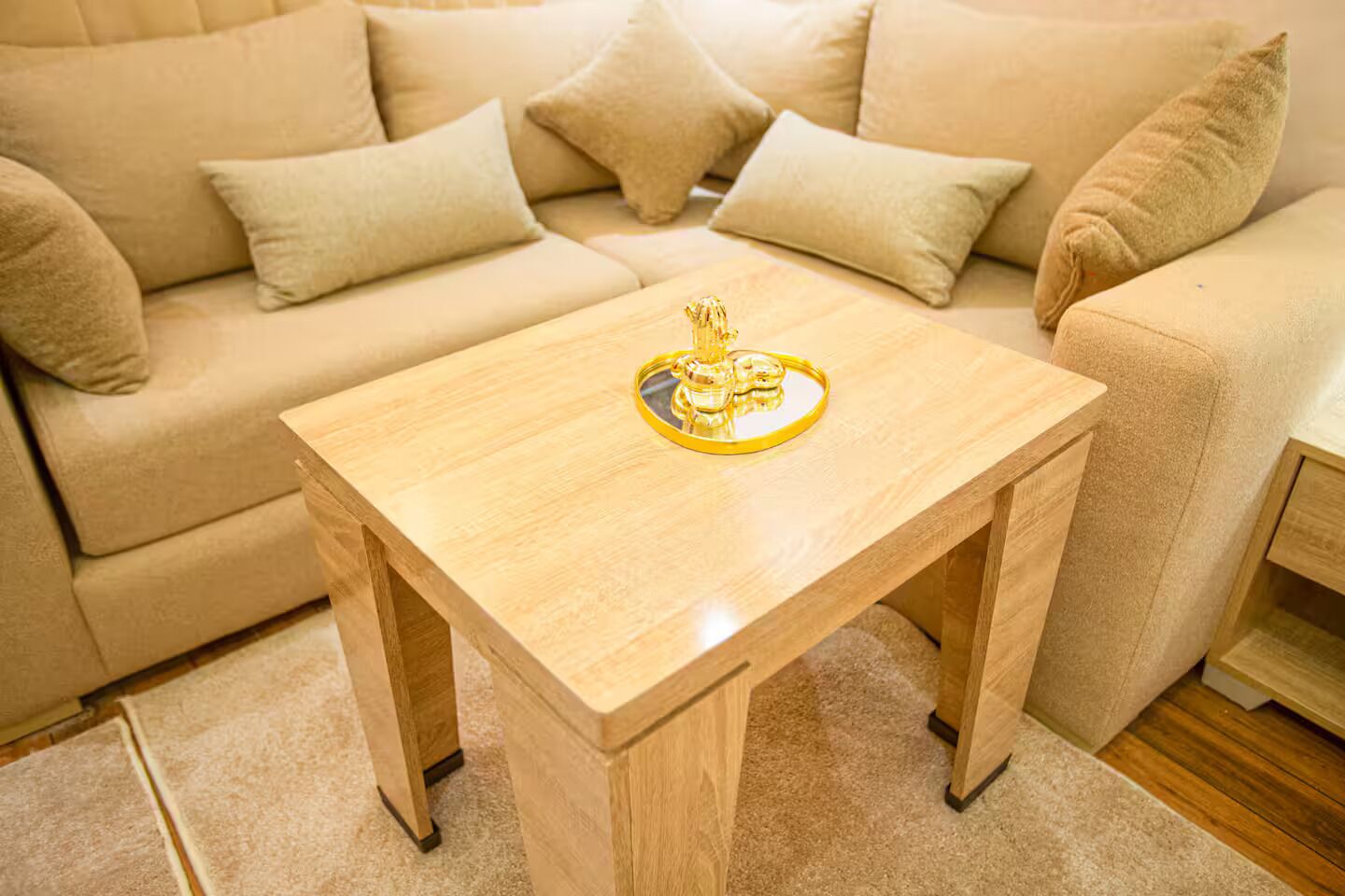 Una sala de estar con un sofá color beige, una mesa de centro de madera y un adorno, además de piso alfombrado.