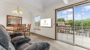 Ein geräumiges Zimmer mit Essbereich, einer großen Glasschiebetür zum Balkon und einem Fernseher, der die Aufschrift 'Grand Welcome' an der Wand zeigt.
