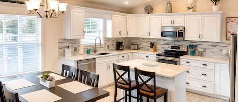 A modern kitchen with white cabinetry, a central island, and a dining area with a dark wooden table and chairs.