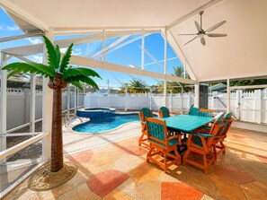 A covered outdoor area with a pool, a table with chairs, and a palm tree.